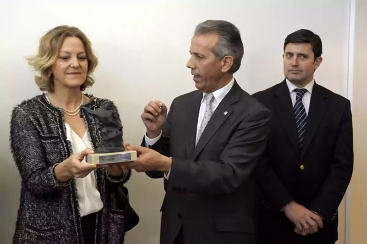 Un hombre entrega un trofeo a una mujer mientras otro hombre observa en el fondo. Un hombre entrega un trofeo a una mujer mientras otro hombre observa en el fondo.