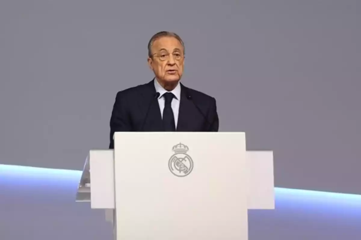 Un hombre de traje oscuro habla desde un podio con el escudo del Real Madrid.