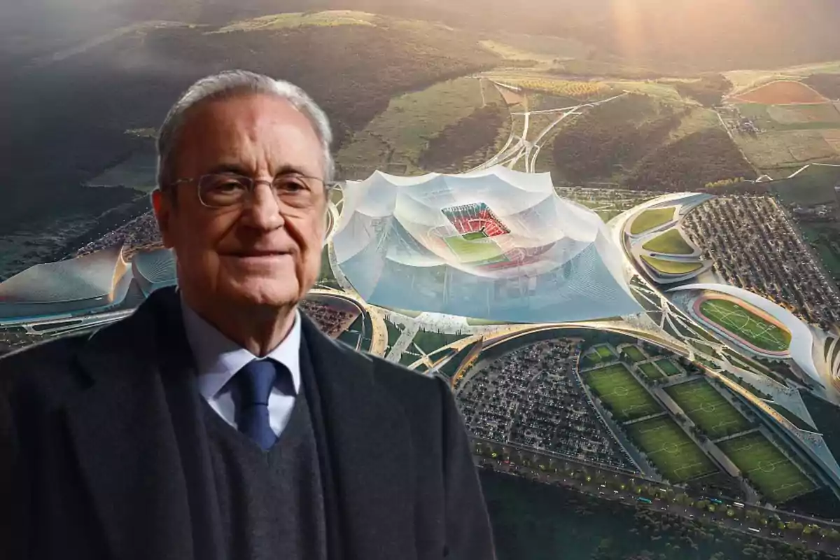 Hombre mayor con gafas y traje oscuro al frente de un estadio futurista rodeado de áreas verdes y canchas deportivas