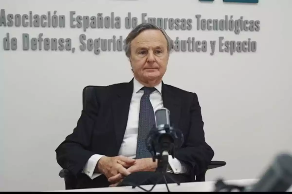 Un hombre con traje y corbata está sentado frente a un micrófono en una sala con un cartel de la Asociación Española de Empresas Tecnológicas de Defensa, Seguridad, Aeronáutica y Espacio. Un hombre con traje y corbata está sentado frente a un micrófono en una sala con un cartel de la Asociación Española de Empresas Tecnológicas de Defensa, Seguridad, Aeronáutica y Espacio.
