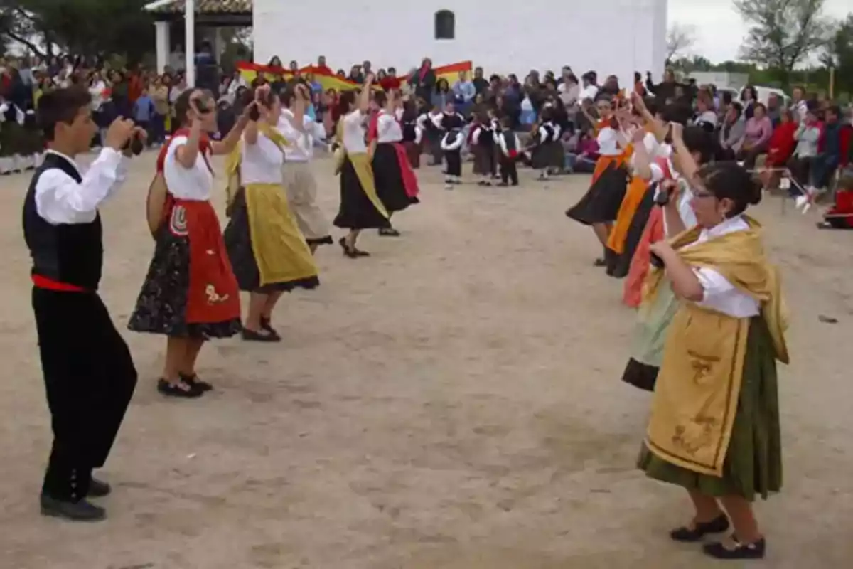 Personas vestidas con trajes tradicionales bailando en un evento al aire libre con una multitud observando.