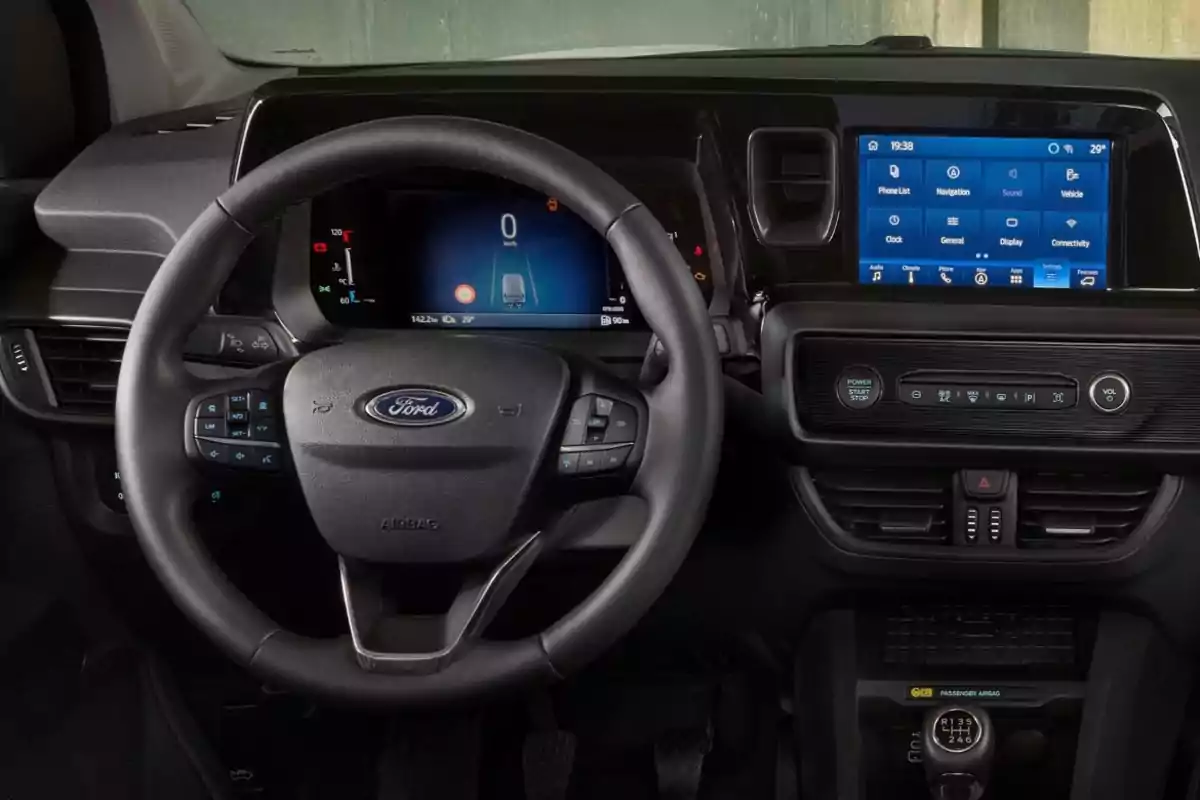 Interior de un automóvil Ford mostrando el volante, el panel de instrumentos digital y la pantalla táctil central con controles de navegación y audio. Interior de un automóvil Ford mostrando el volante, el panel de instrumentos digital y la pantalla táctil central con controles de navegación y audio.