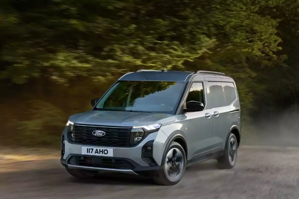 Una furgoneta gris de la marca Ford circulando por un camino rodeado de árboles.