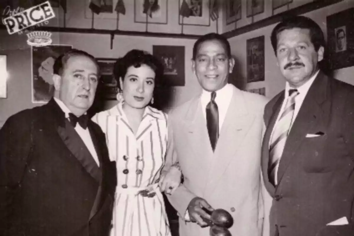 Un grupo de cuatro personas posando en un evento formal en un lugar decorado con fotografías en la pared.