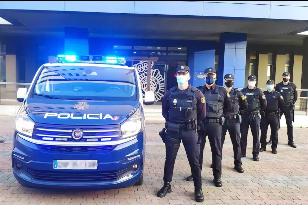 Un grupo de policías con mascarillas posando frente a una camioneta policial azul con luces encendidas.