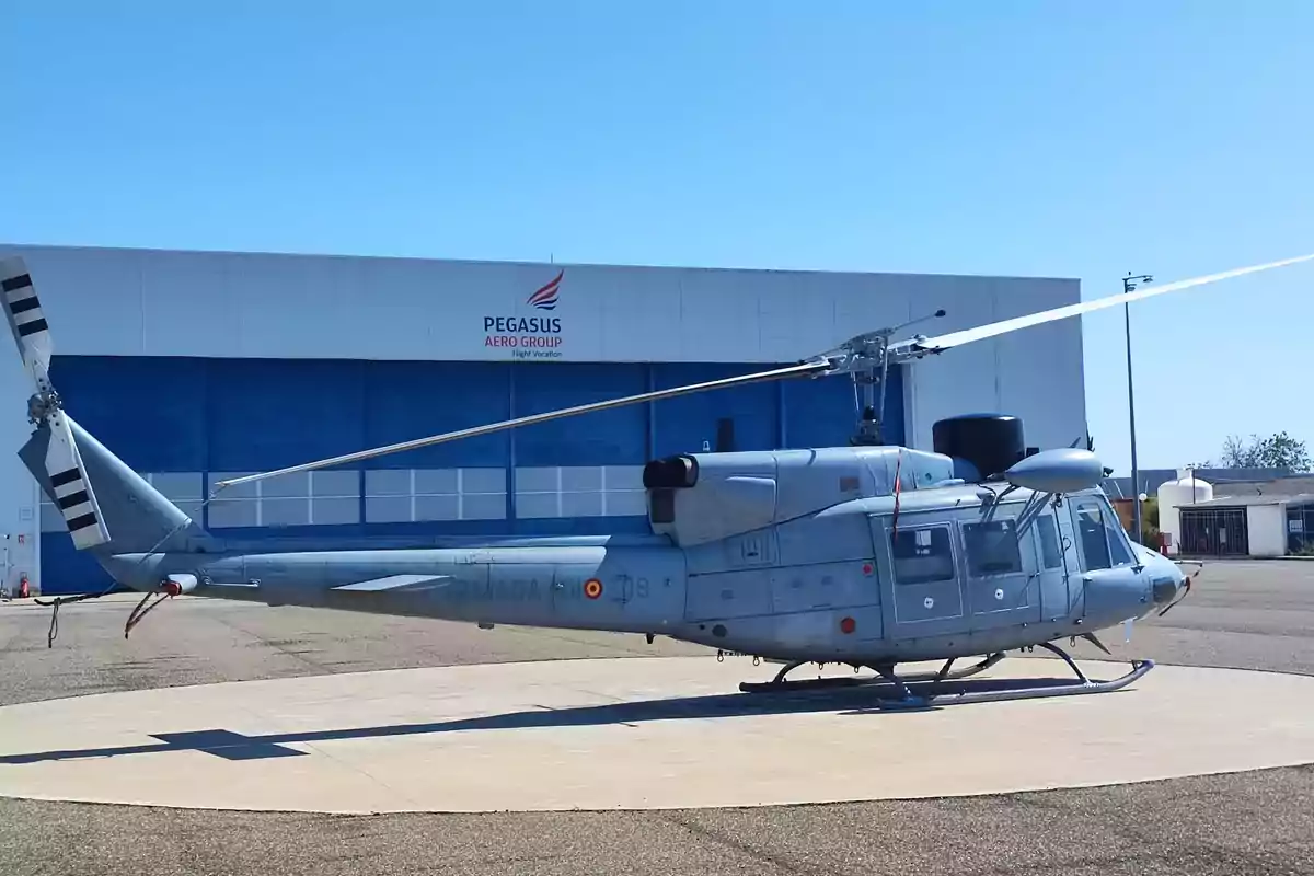 Helicóptero militar estacionado en una plataforma frente a un hangar de Pegasus Aero Group.