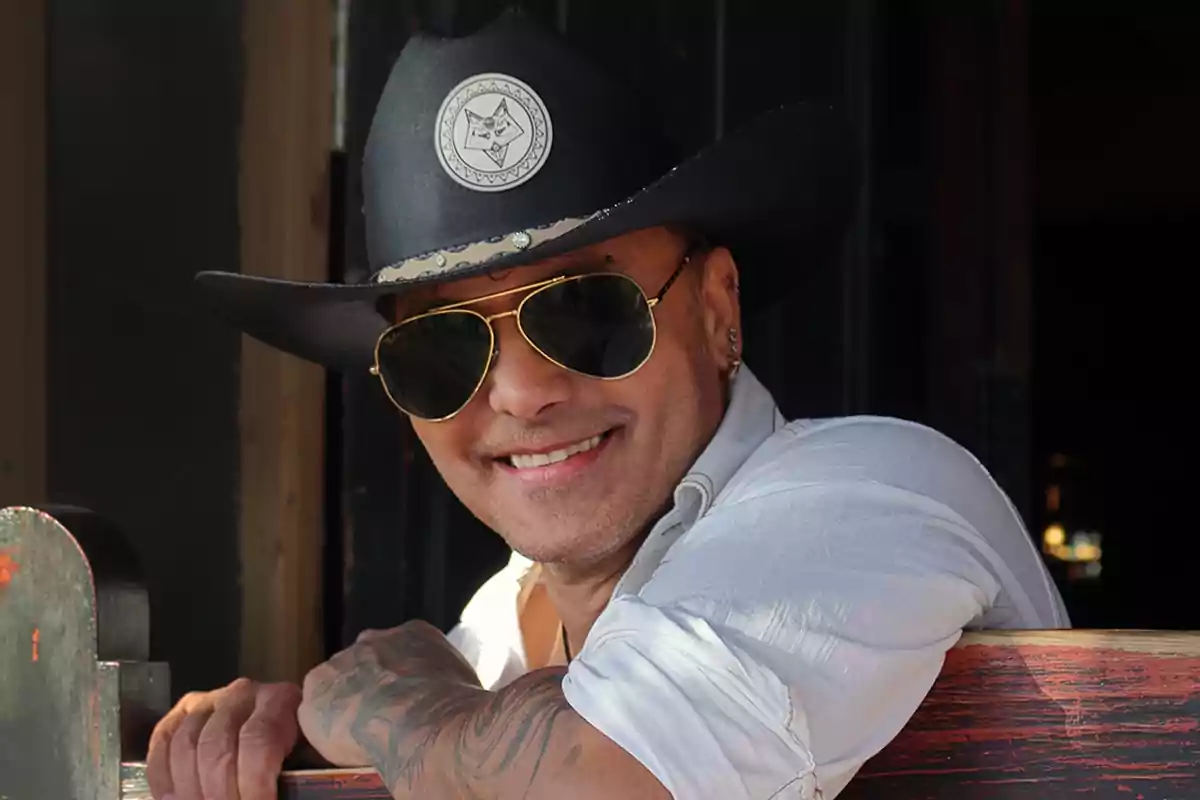 Un hombre sonriente con sombrero de vaquero y gafas de sol.