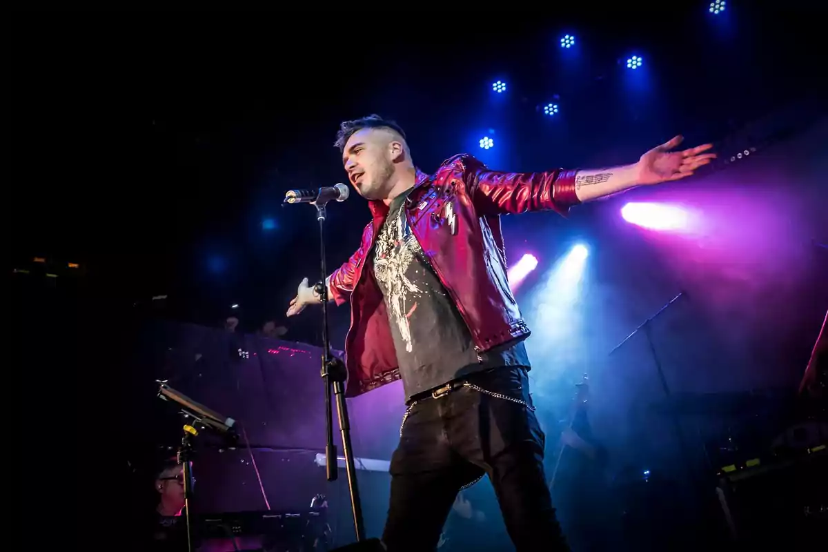 Cantante con chaqueta roja interpretando una canción en el escenario con luces de colores de fondo