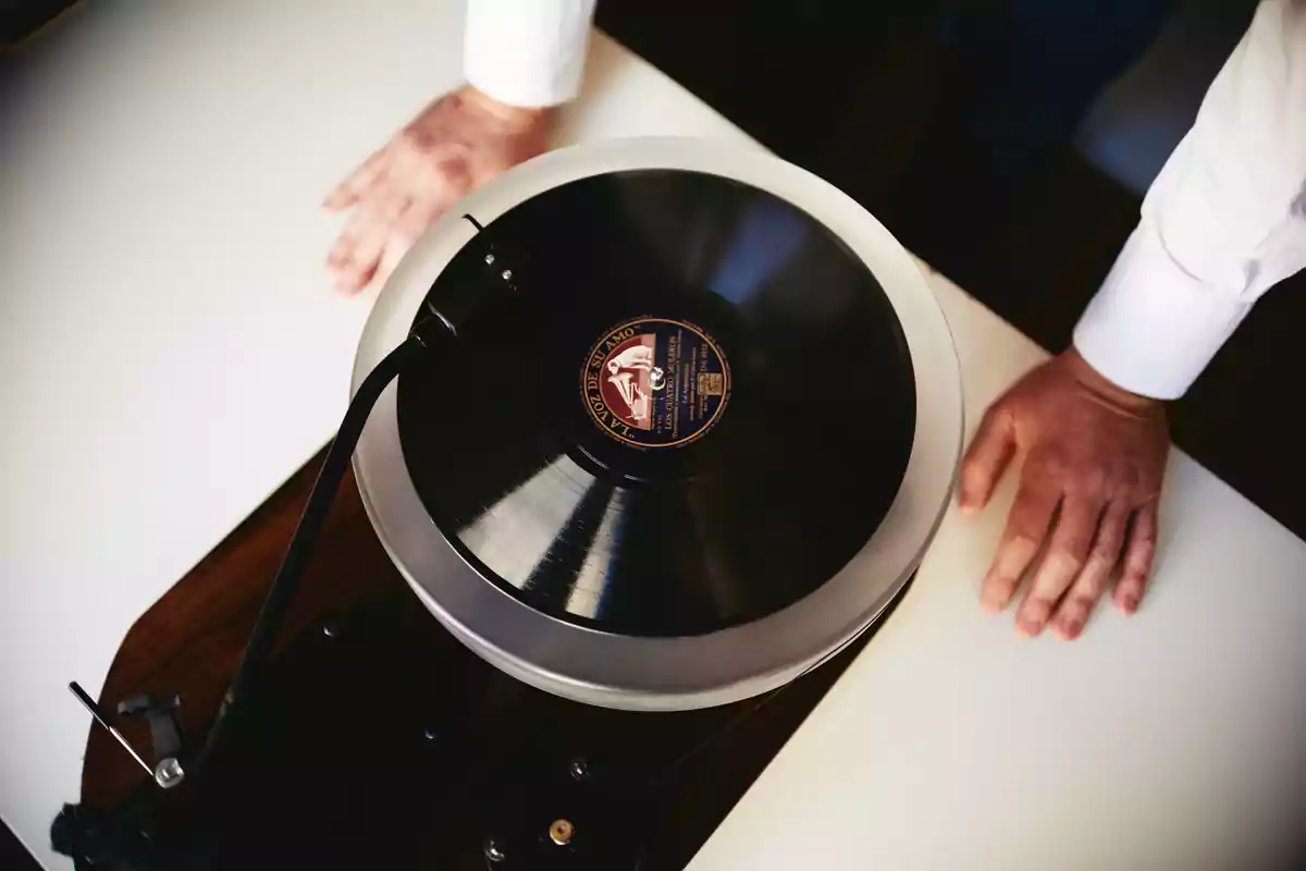 Persona con camisa blanca manipulando un tocadiscos con un disco de vinilo.