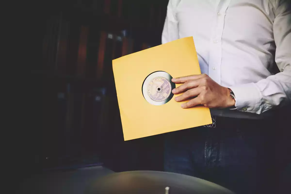 Persona sosteniendo un disco de vinilo en una funda amarilla.