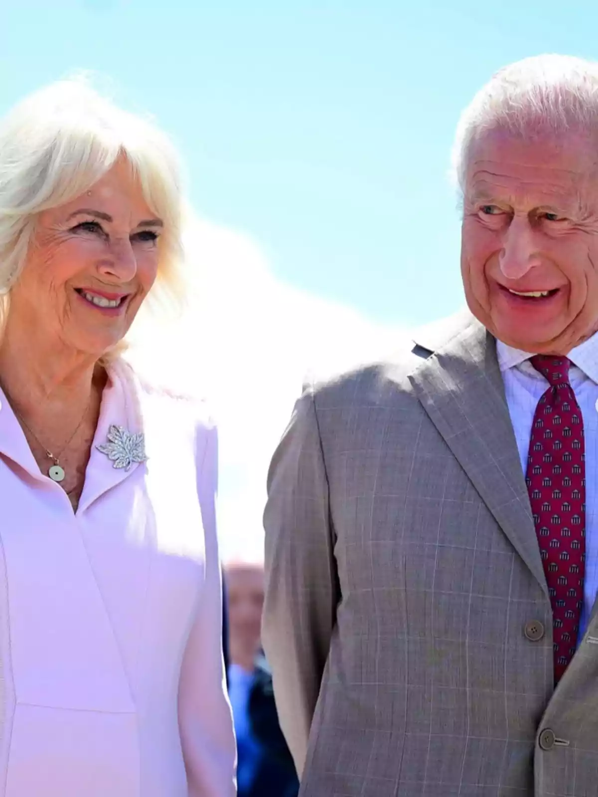 El rey Carlos III y la reina consorte Camila sonríen mientras están de pie al aire libre bajo un cielo azul El rey Carlos III y la reina consorte Camila sonríen mientras están de pie al aire libre bajo un cielo azul