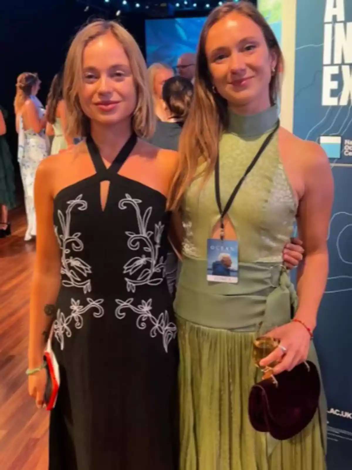 Marina Windsor posa sonriente junto a una mujer en un evento elegante, ella lleva un vestido negro con detalles blancos y Marina un vestido verde claro, ambas están abrazadas y rodeadas de otras personas en un ambiente iluminado Marina Windsor posa sonriente junto a una mujer en un evento elegante, ella lleva un vestido negro con detalles blancos y Marina un vestido verde claro, ambas están abrazadas y rodeadas de otras personas en un ambiente iluminado