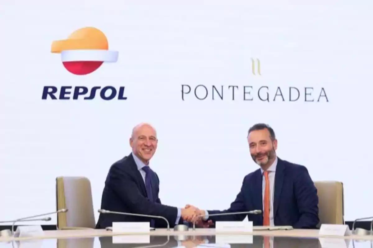 Dos hombres estrechando manos en una mesa con los logotipos de Repsol y Pontegadea en el fondo.
