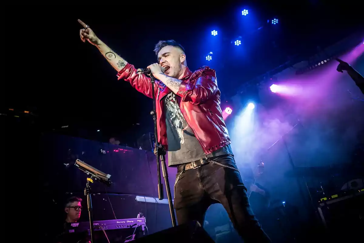 Cantante con chaqueta roja interpretando una canción en el escenario con luces de colores y ambiente de concierto