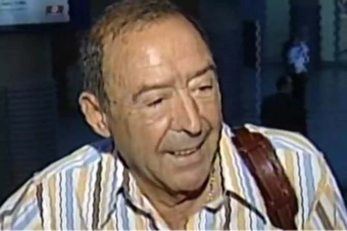 Un hombre mayor con camisa de rayas sonríe mientras mira hacia un lado en un entorno interior. Un hombre mayor con camisa de rayas sonríe mientras mira hacia un lado en un entorno interior.