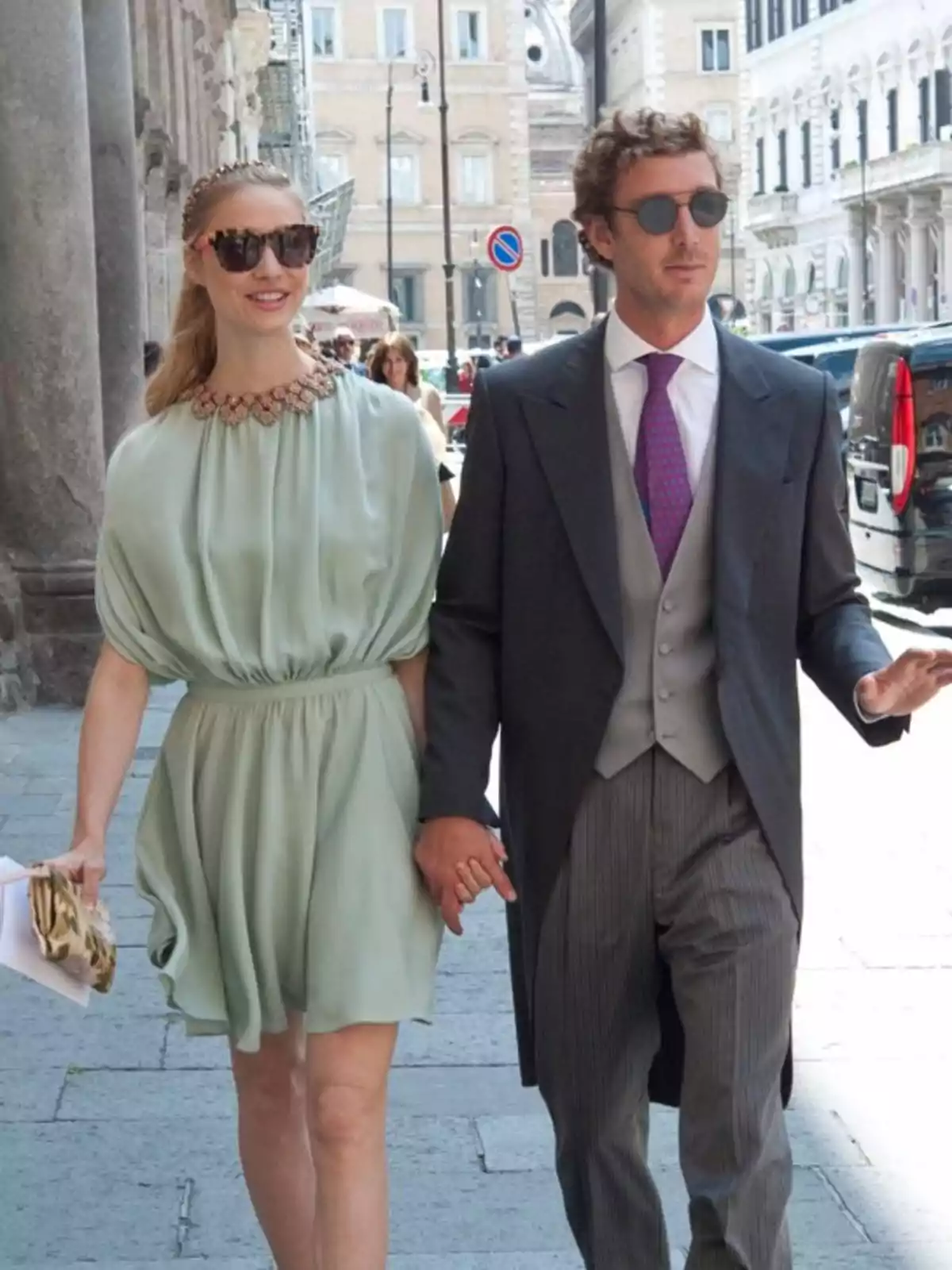 Una pareja caminando por una calle elegante, ambos con gafas de sol; ella lleva un vestido verde claro y él viste un traje formal con chaleco y corbata morada. Una pareja caminando por una calle elegante, ambos con gafas de sol; ella lleva un vestido verde claro y él viste un traje formal con chaleco y corbata morada.
