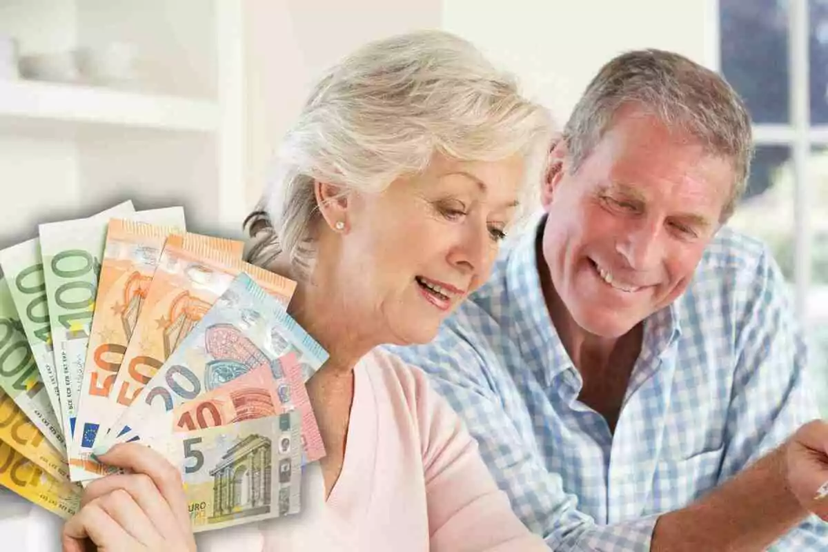 Pareja de personas mayores sonriendo mientras revisan documentos con billetes de euro en la mano.