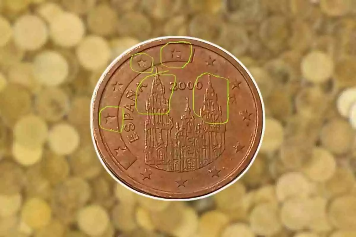 Moneda de un céntimo de euro de España del año 2000 con la Catedral de Santiago de Compostela en el centro y estrellas alrededor sobre un fondo de monedas desenfocadas.