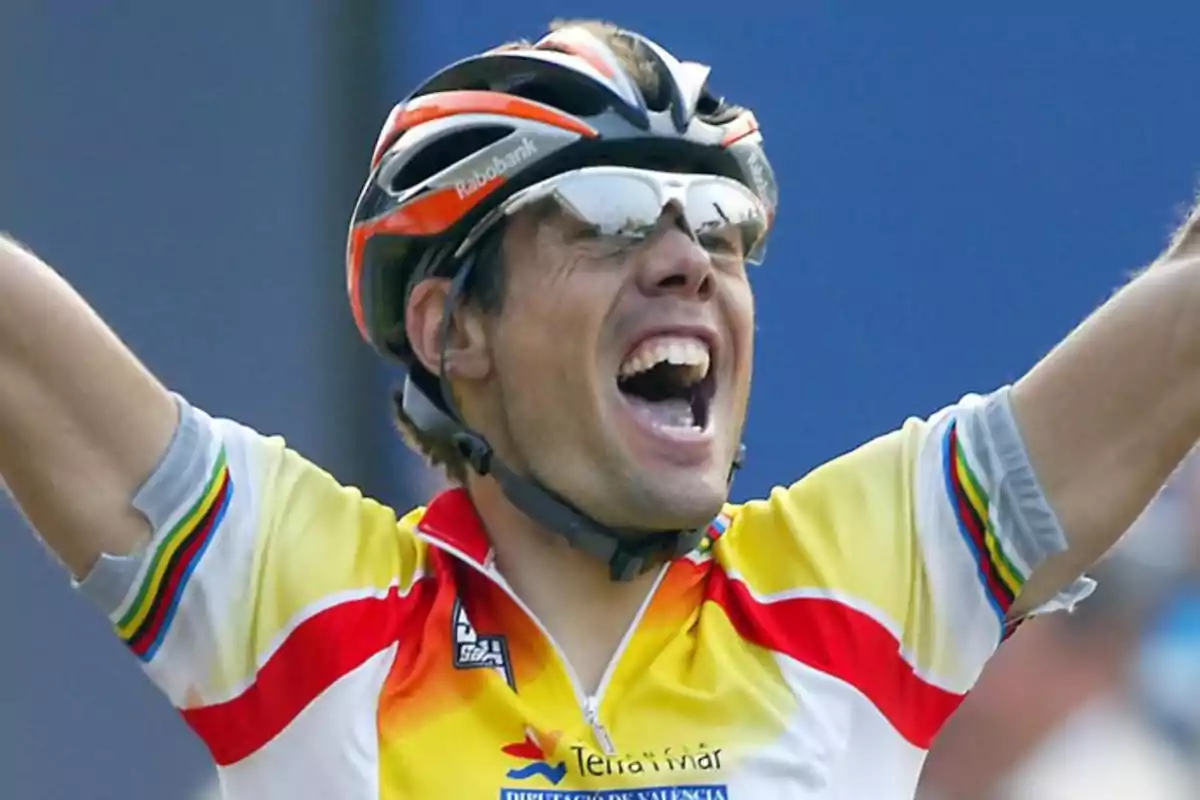 Un ciclista celebrando con los brazos en alto, vistiendo un uniforme colorido y un casco.