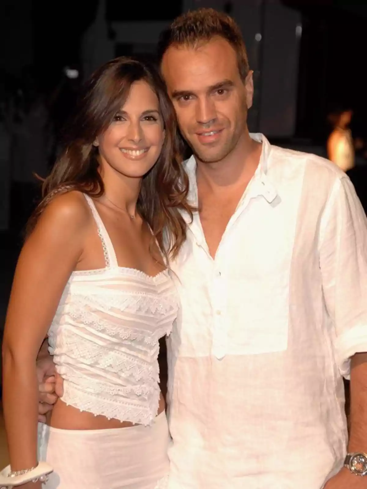 Pareja joven sonriendo y posando juntos, ambos vestidos de blanco en un ambiente nocturno Pareja joven sonriendo y posando juntos, ambos vestidos de blanco en un ambiente nocturno