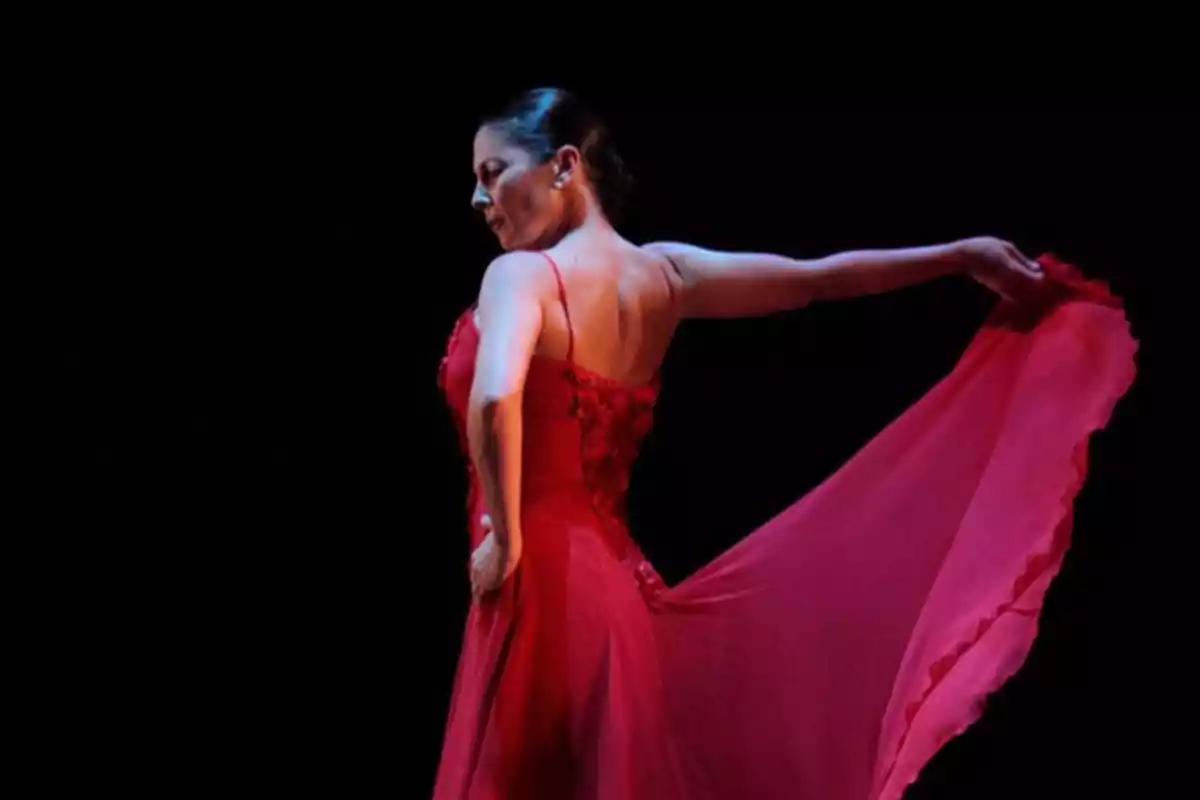 Bailarina con vestido rojo en pose de danza sobre un fondo oscuro.