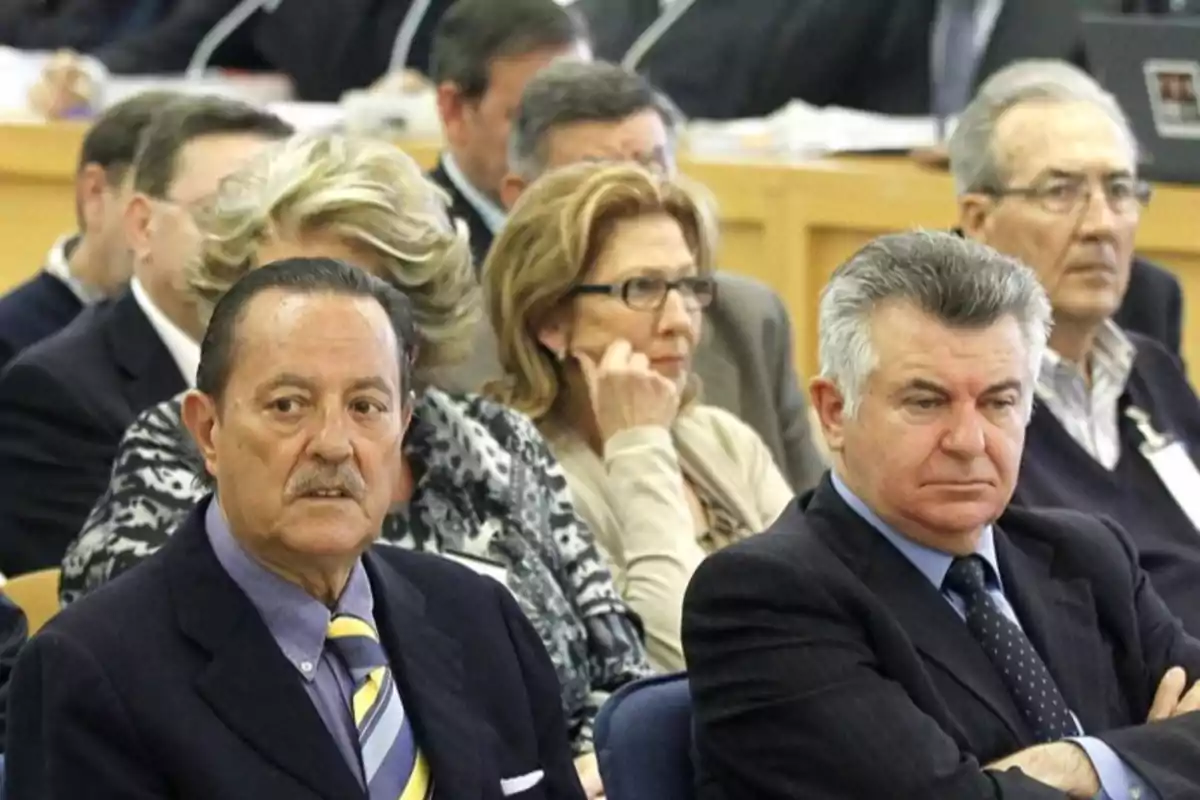 Un grupo de personas mayores sentadas en una sala, algunas con expresión seria, posiblemente en un evento formal o reunión. Un grupo de personas mayores sentadas en una sala, algunas con expresión seria, posiblemente en un evento formal o reunión.