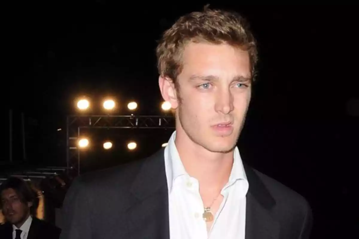Un hombre con traje oscuro y camisa blanca está de pie frente a luces brillantes en un entorno nocturno. Un hombre con traje oscuro y camisa blanca está de pie frente a luces brillantes en un entorno nocturno.