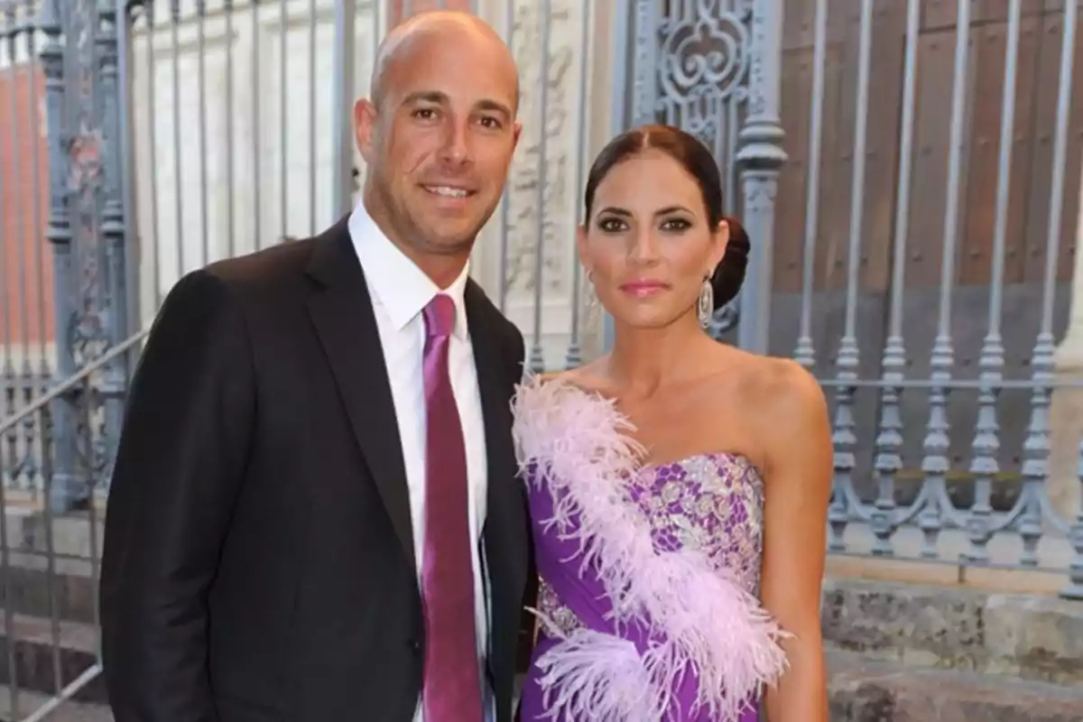 Una pareja elegantemente vestida posa frente a una puerta de hierro forjado. Una pareja elegantemente vestida posa frente a una puerta de hierro forjado.