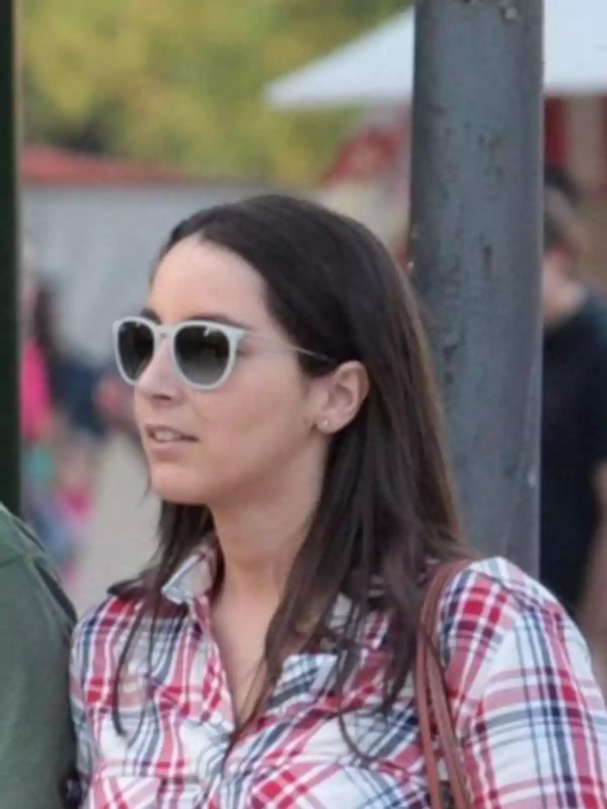 Una persona con gafas de sol y camisa a cuadros está de pie al aire libre. Una persona con gafas de sol y camisa a cuadros está de pie al aire libre.