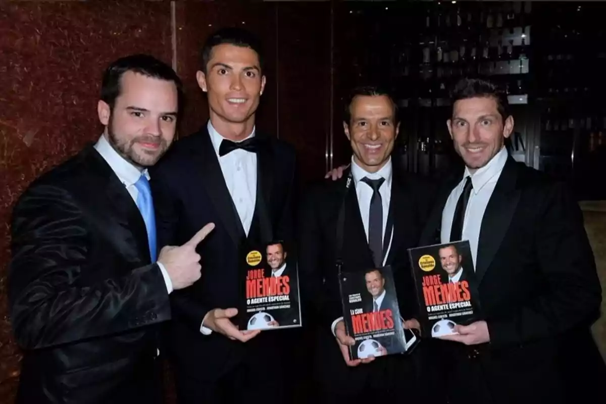 Cuatro hombres vestidos de traje posan juntos sosteniendo libros en un evento.