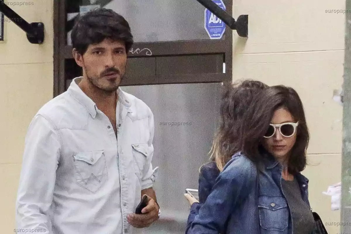 Un hombre con camisa clara y una mujer con gafas de sol y chaqueta de mezclilla caminan juntos por la calle. Un hombre con camisa clara y una mujer con gafas de sol y chaqueta de mezclilla caminan juntos por la calle.