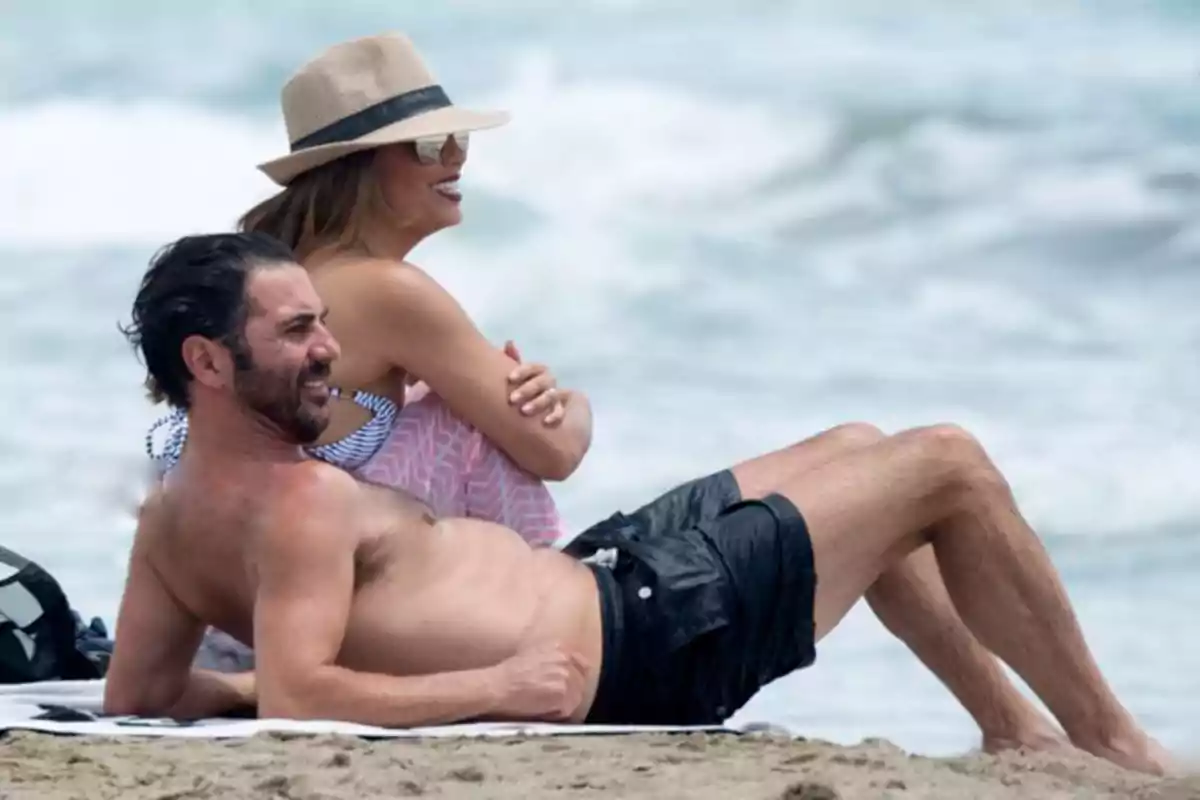 Pareja disfrutando de un día en la playa sentados sobre la arena frente al mar Pareja disfrutando de un día en la playa sentados sobre la arena frente al mar