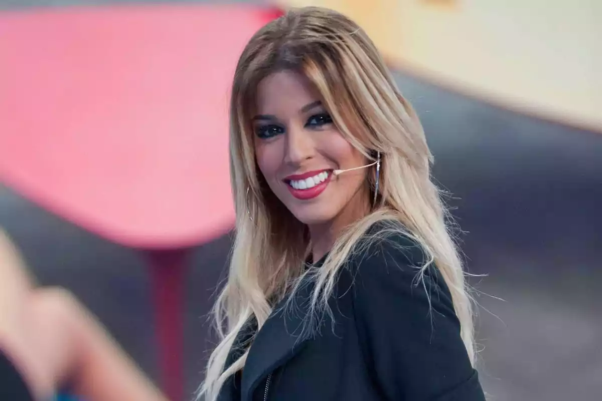 Una mujer sonriente con cabello rubio y largo usando un micrófono de diadema y aretes grandes.