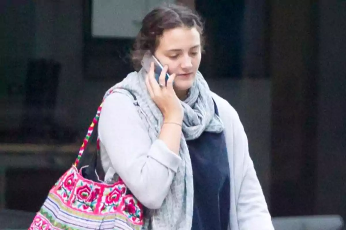 Mujer joven caminando mientras habla por teléfono y lleva una bolsa colorida al hombro Mujer joven caminando mientras habla por teléfono y lleva una bolsa colorida al hombro