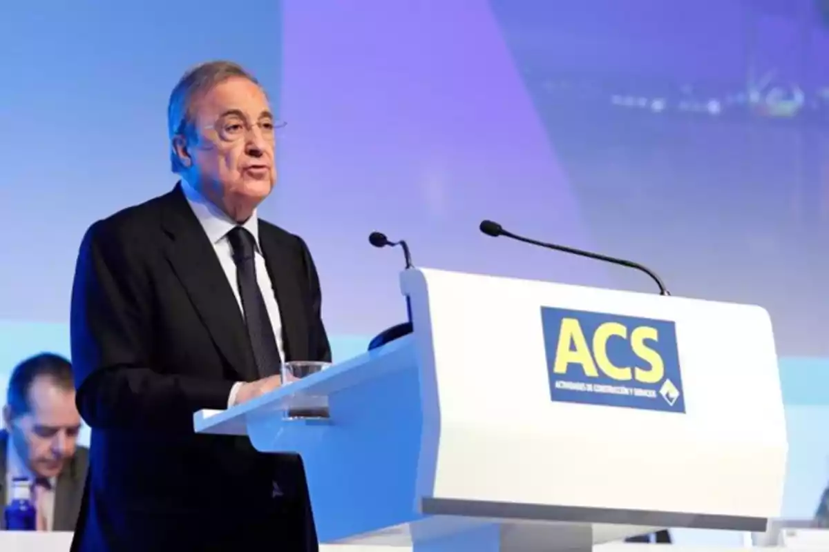 Hombre mayor de traje hablando en un podio con el logo de ACS en un evento empresarial
