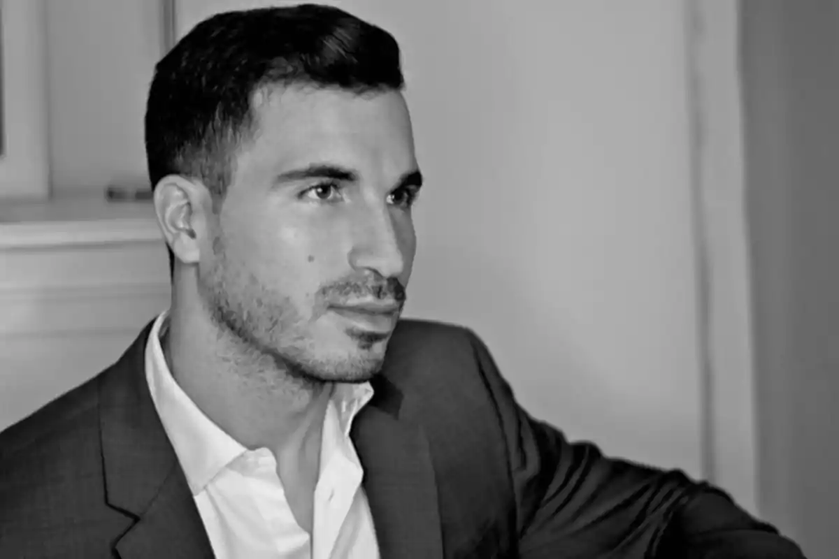 Un hombre con barba y cabello corto viste un traje y mira hacia un lado en una fotografía en blanco y negro.