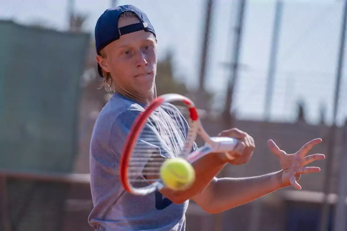 Un jugador de tenis golpea una pelota con su raqueta en una cancha al aire libre.