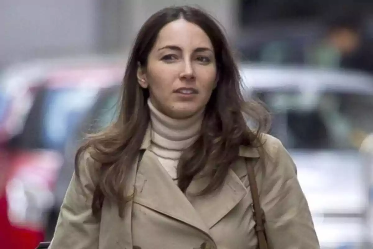Una mujer con cabello largo y castaño lleva un abrigo beige y un suéter de cuello alto mientras camina por una calle urbana. Una mujer con cabello largo y castaño lleva un abrigo beige y un suéter de cuello alto mientras camina por una calle urbana.