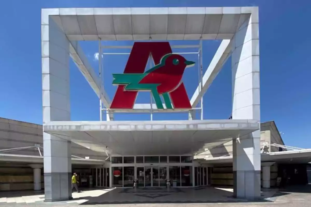 Entrada de un centro comercial con un gran logotipo de un pájaro rojo y verde sobre una letra A en la parte superior de la estructura.