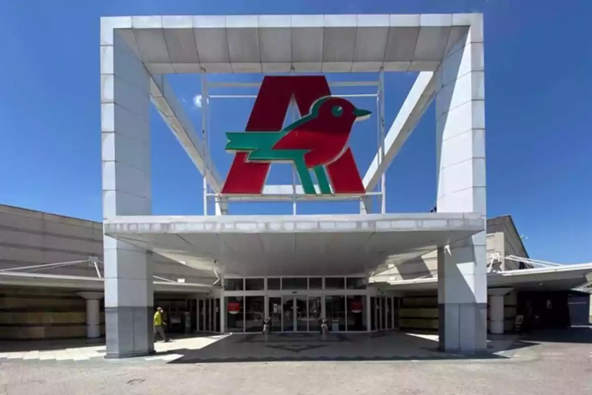 Entrada de un centro comercial con un gran logotipo de un pájaro rojo y verde sobre una letra A en la parte superior de la estructura.