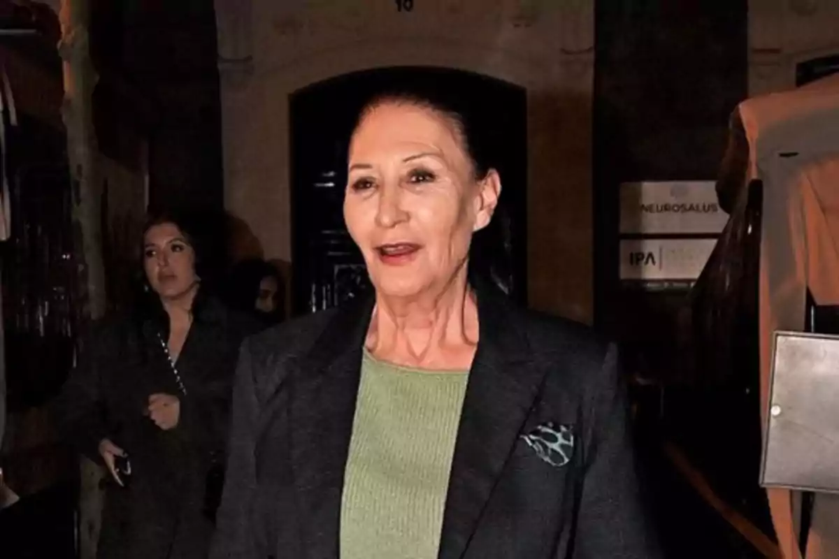 Mujer de cabello oscuro recogido vestida con suéter verde y saco oscuro caminando de noche por la calle Mujer de cabello oscuro recogido vestida con suéter verde y saco oscuro caminando de noche por la calle