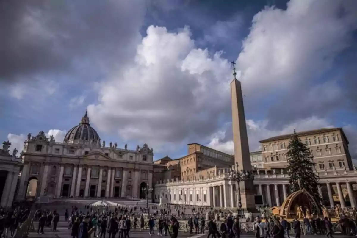 Una multitud de personas camina por la Plaza de San Pedro en el Vaticano con la Basílica de San Pedro y un obelisco al fondo bajo un cielo nublado. Una multitud de personas camina por la Plaza de San Pedro en el Vaticano con la Basílica de San Pedro y un obelisco al fondo bajo un cielo nublado.