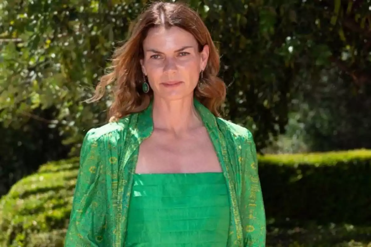 Mujer con vestido verde posando al aire libre con un fondo de vegetación.