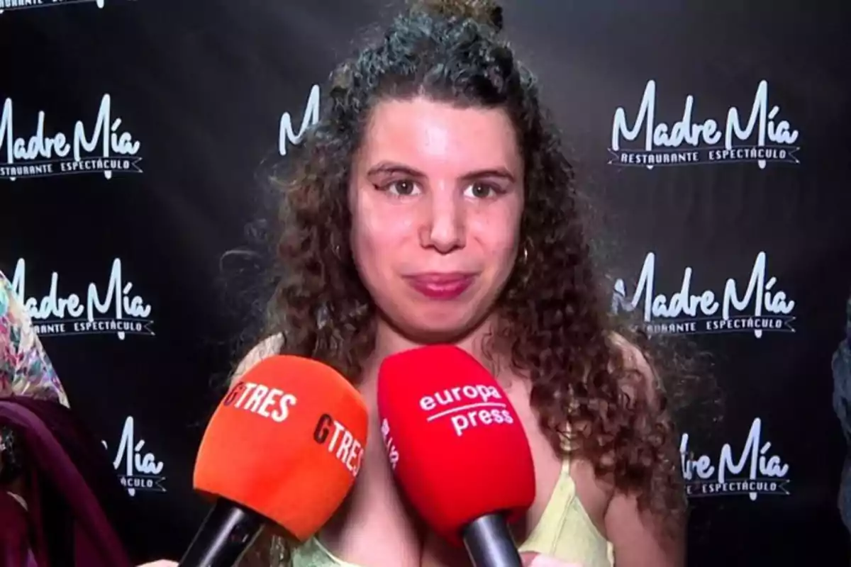 Una mujer con cabello rizado está siendo entrevistada por varios medios de comunicación, sosteniendo micrófonos de GTRES y Europa Press, con un fondo que muestra el logo de 