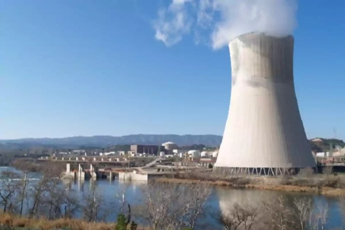 Planta de energía nuclear con torre de enfriamiento y vapor saliendo al cielo azul.