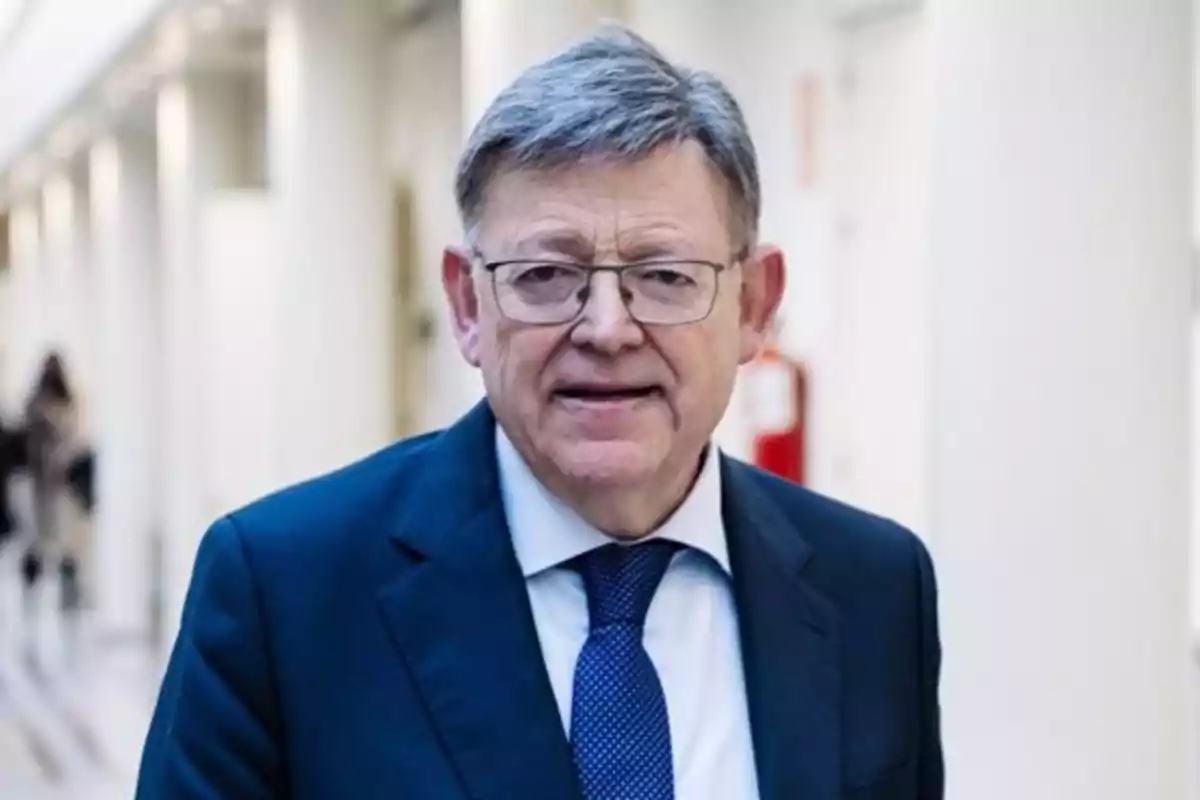 Un hombre con gafas y traje azul oscuro en un pasillo iluminado. Un hombre con gafas y traje azul oscuro en un pasillo iluminado.