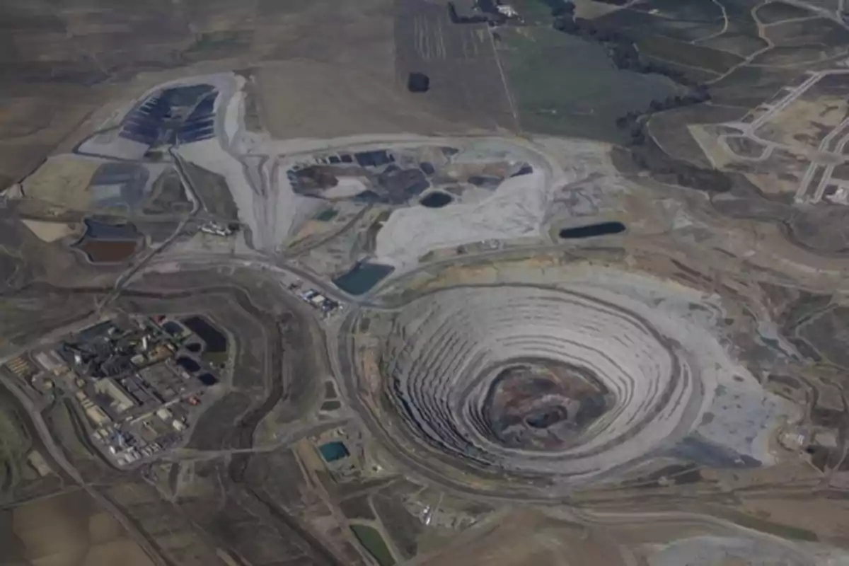 Vista aérea de una mina a cielo abierto con áreas de excavación y estructuras industriales circundantes.