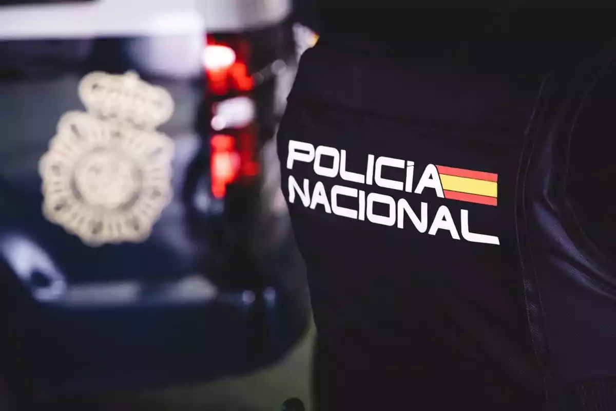 Chaleco de un agente de la Policía Nacional de España junto a un vehículo policial desenfocado Chaleco de un agente de la Policía Nacional de España junto a un vehículo policial desenfocado