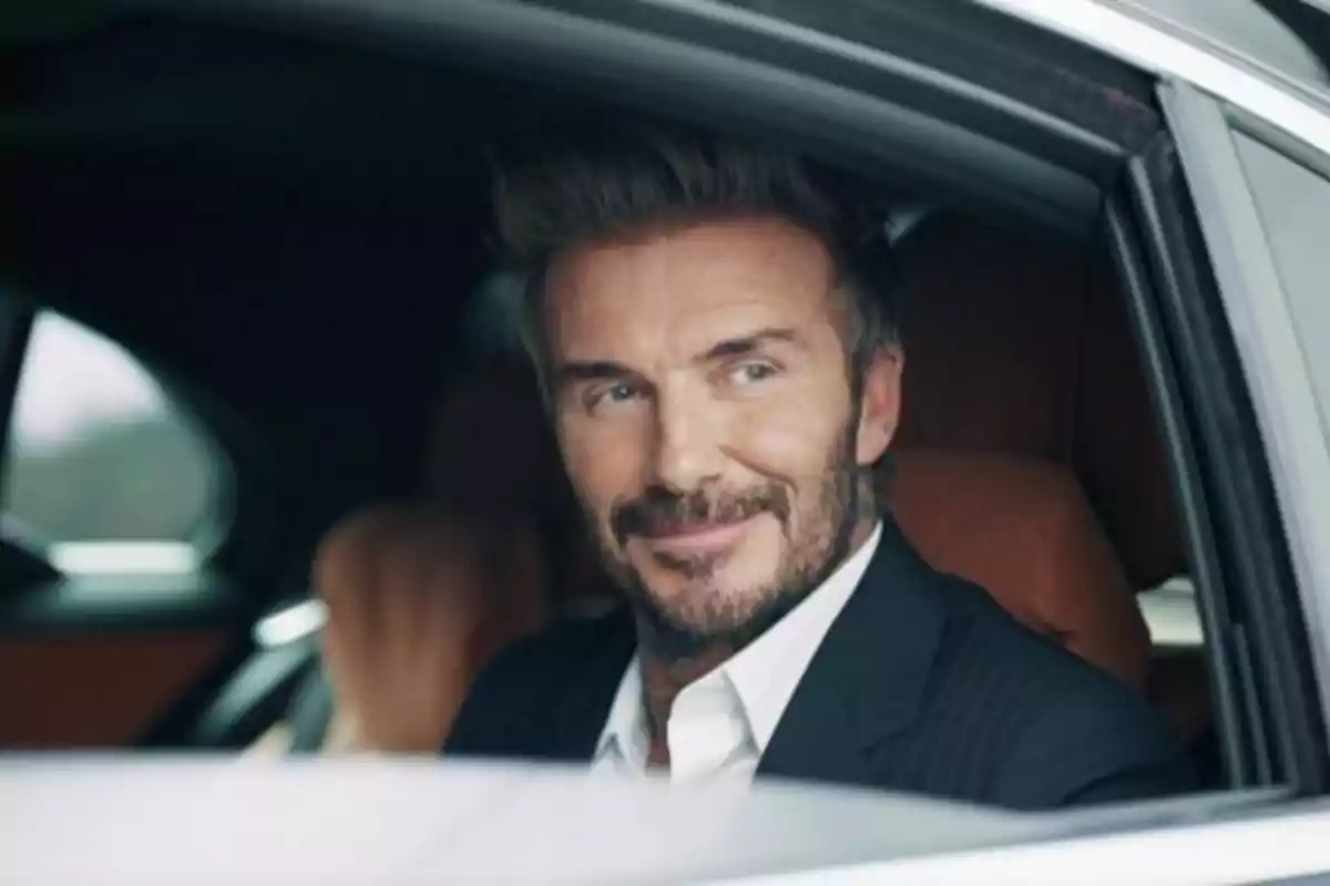 Hombre con barba y traje sentado en el asiento trasero de un automóvil mirando hacia afuera por la ventana con una expresión sonriente Hombre con barba y traje sentado en el asiento trasero de un automóvil mirando hacia afuera por la ventana con una expresión sonriente