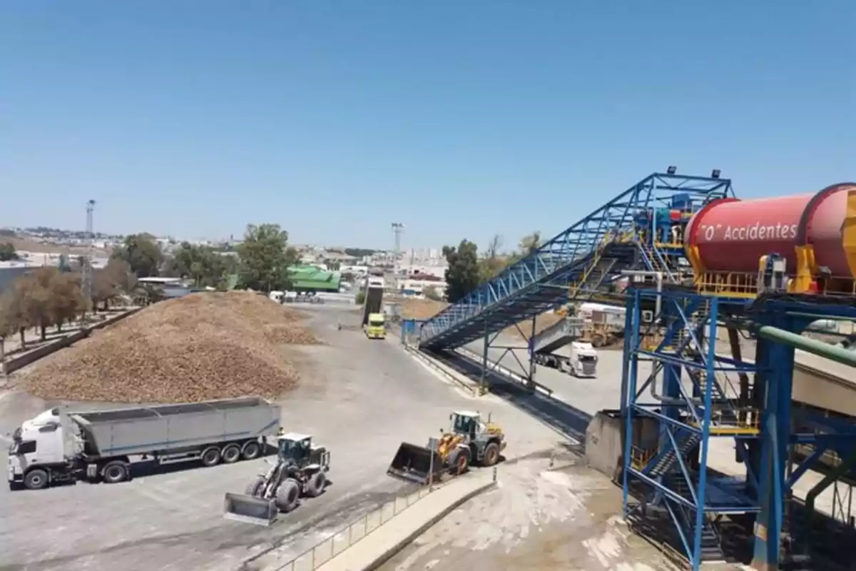 Una planta industrial con maquinaria pesada, montones de material y un letrero que promueve la seguridad laboral. Una planta industrial con maquinaria pesada, montones de material y un letrero que promueve la seguridad laboral.